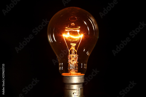 Clear glass electric lightbulb dimmed to enable it's tungsten filament to be seen isolated on a black background