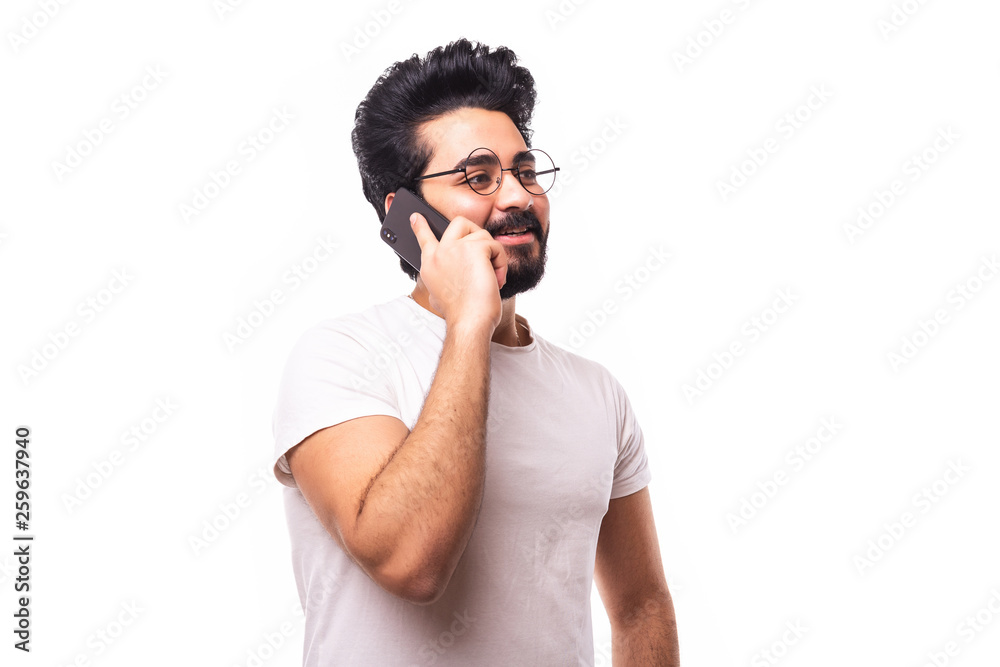 Portrait of happy young bearded emotional arab man standing over white wall background isolated. Looking aside while talking by phone. Portrait of happy young bearded emotional arab man standing over white wall background isolated. Looking aside while talking by phone.