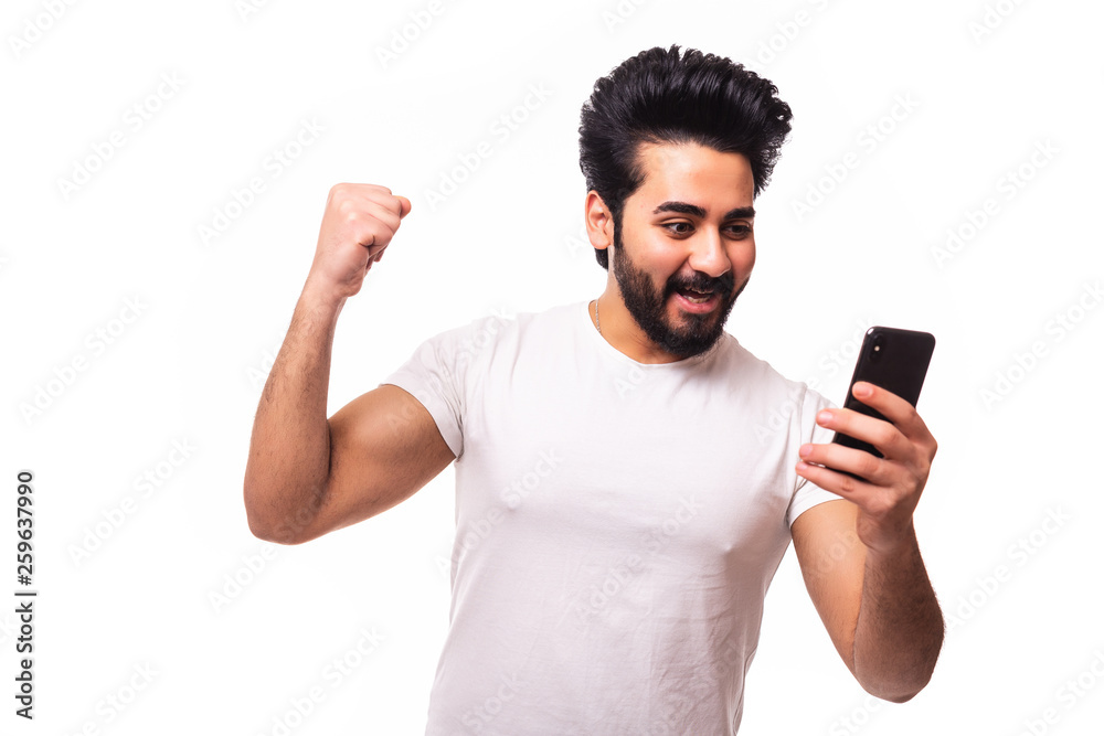 Portrait of an excited young arab man celebrating looking at mobile phone isolated over white background Portrait of an excited young arab man celebrating looking at mobile phone isolated over white background