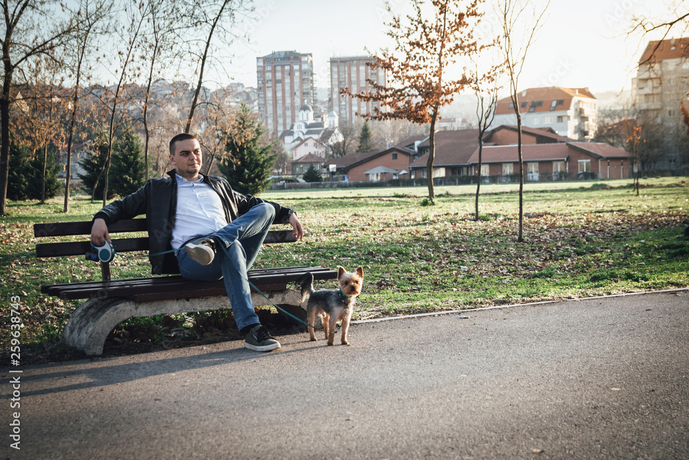 Young man with small cute dog sitting at park and enjoying the sun Young man with small cute dog sitting at park and enjoying the sun