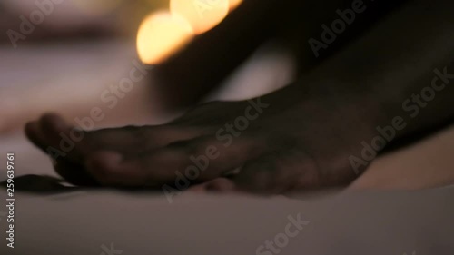 Closeup of female hands in intimate moment of having sex covered with dark-skinned male hands during orgasm. Diverse passionate couple making love in romantic atmoshere of candlelit bedroom