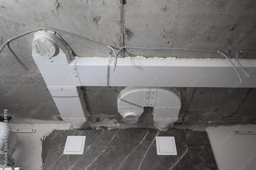 Integrated built-in air conditioning system on the concrete ceiling in the bathroom. White plastic air boxes laying on the ceiling. Repair in bathroom. Unfinished interior. Integrated built-in air conditioning system on the concrete ceiling in the bathroom. White plastic air boxes laying on the ceiling. Repair in bathroom. Unfinished interior.