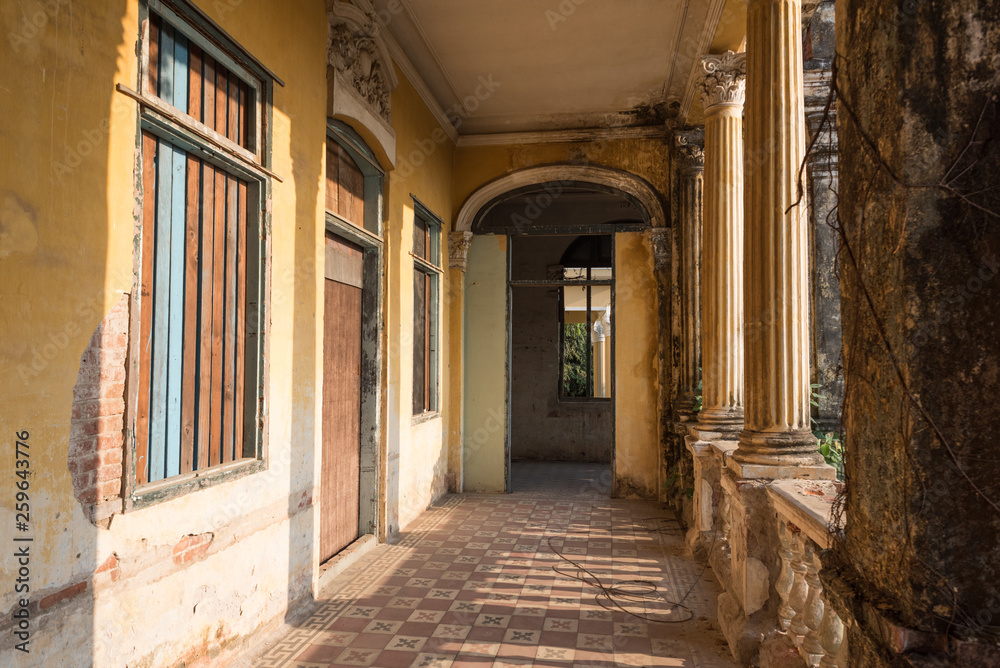 Passage with tiled floor and boarded-up windows along columns on the second floor of the Mansion or Villa Bodega, a half-ruined colonial-era building (1910-1920s) in Phnom Penh city center, Cambodia.