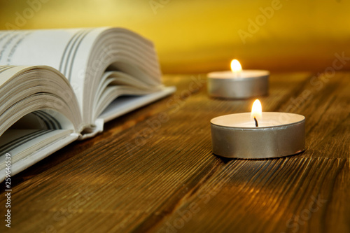 An open book about religion and faith lies on wooden planks on a golden background. Nearby are lit candles