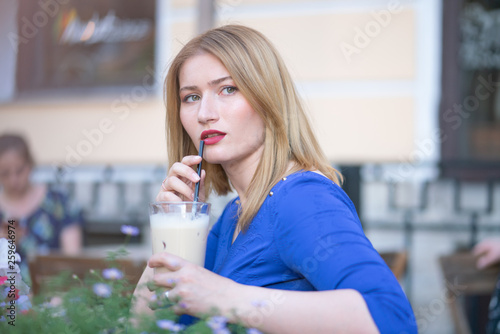 charming caucasian blonde girl in a blue dress sitting at a table in a city cafe alone and waiting