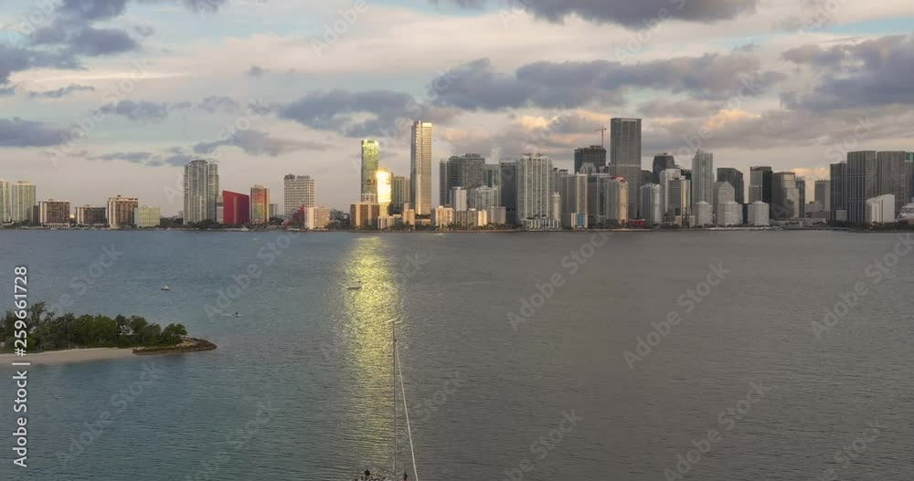 Slow motion shot of a drone flying over a sailboat in the Miami South Channel towards the Brickell skyline on an afternoon with the sun reflecting onto the water aligned with the boat near an island Slow motion shot of a drone flying over a sailboat in the Miami South Channel towards the Brickell skyline on an afternoon with the sun reflecting onto the water aligned with the boat near an island