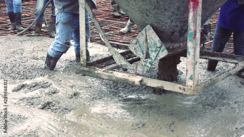 Man worker using a concrete steel basket for cement after Pouring ready-mixed concrete on steel reinforcement to make the road by mixing mobile the concrete mixer. Man worker using a concrete steel basket for cement after Pouring ready-mixed concrete on steel reinforcement to make the road by mixing mobile the concrete mixer.
