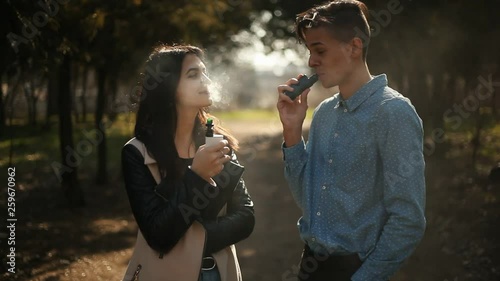 handsome vaping man talking with beautiful vaping girl in the park