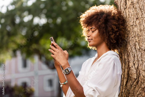 Outdoor portrait of a Young black African American young woman texting on mobile phone