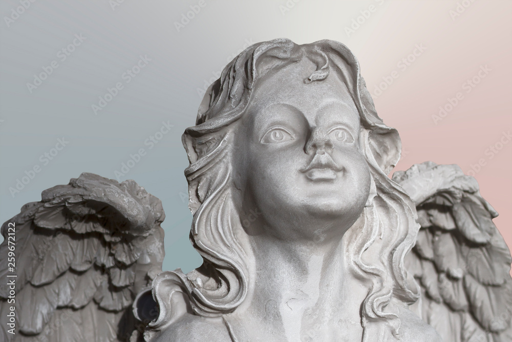 Statue of a white stone praying angel on pastel backgrouond, face and wings close-up. Selective focus