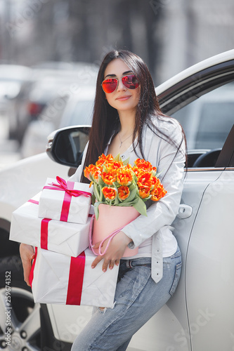 Young attractive woman holding presents. Girl in the car. Stylish lady outdoor. photo