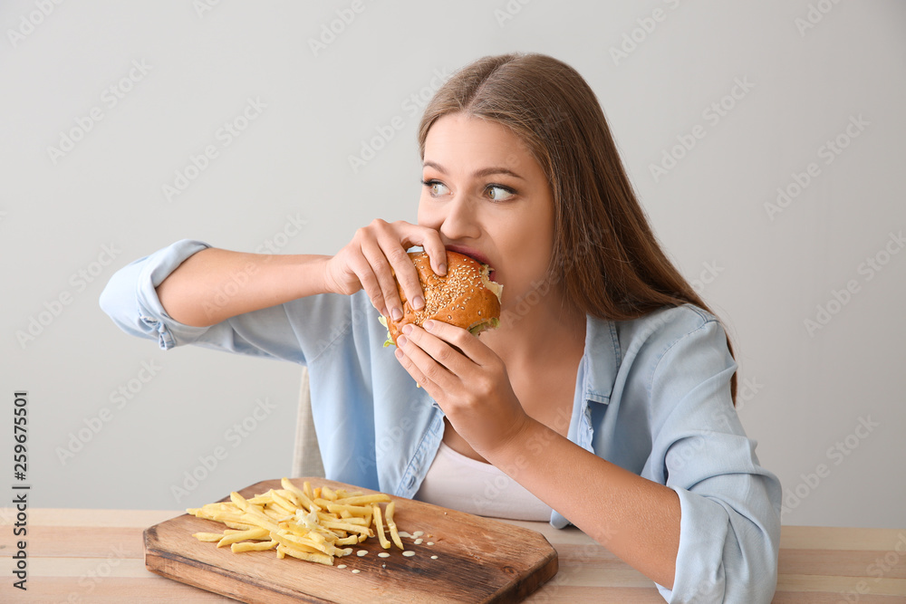 Young woman eating tasty burger with french fries at table Young woman eating tasty burger with french fries at table