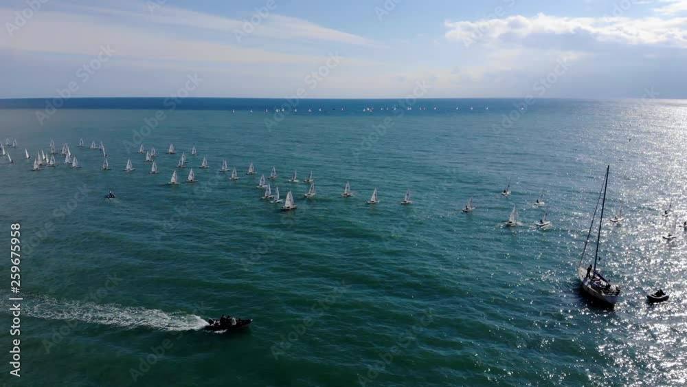 Aerial fly around many sailboats in sea during regatta. Sunny day, blue sea. Start of regatta in Sochi. Aerial fly around many sailboats in sea during regatta. Sunny day, blue sea. Start of regatta in Sochi.
