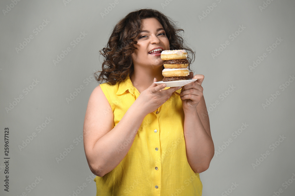 Overweight woman with donuts on grey background