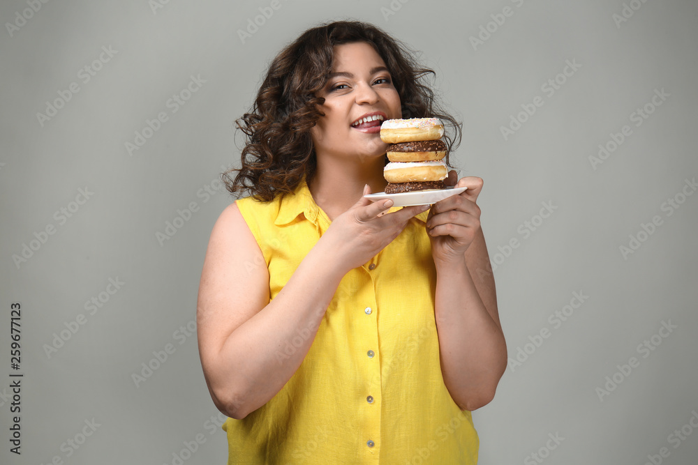 Overweight woman with donuts on grey background Overweight woman with donuts on grey background