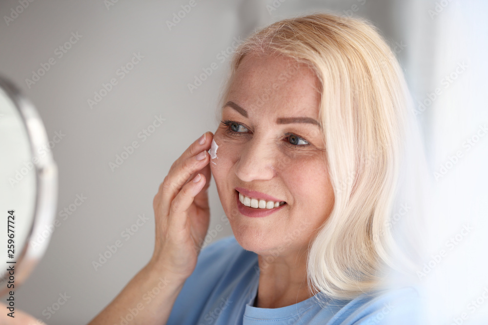 Mature woman applying facial cream at home Mature woman applying facial cream at home
