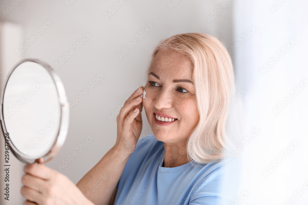 Mature woman applying facial cream at home Mature woman applying facial cream at home