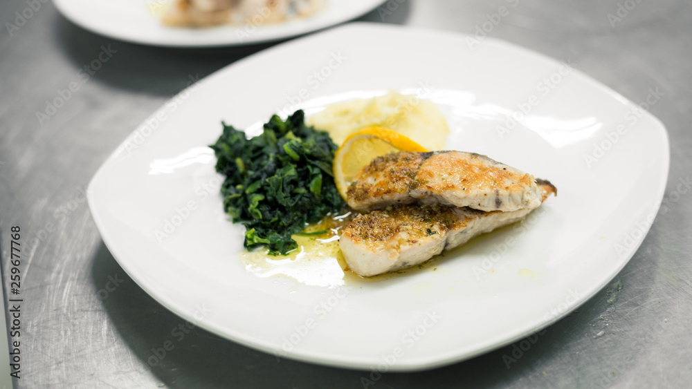 salmon steak grilled with mash potato and spinach in restaurant kitchen