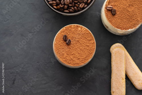 Delicious Italian dessert tiramisu, chocolate, cocoa and coffee beans on a black background. Top view with copy space.
