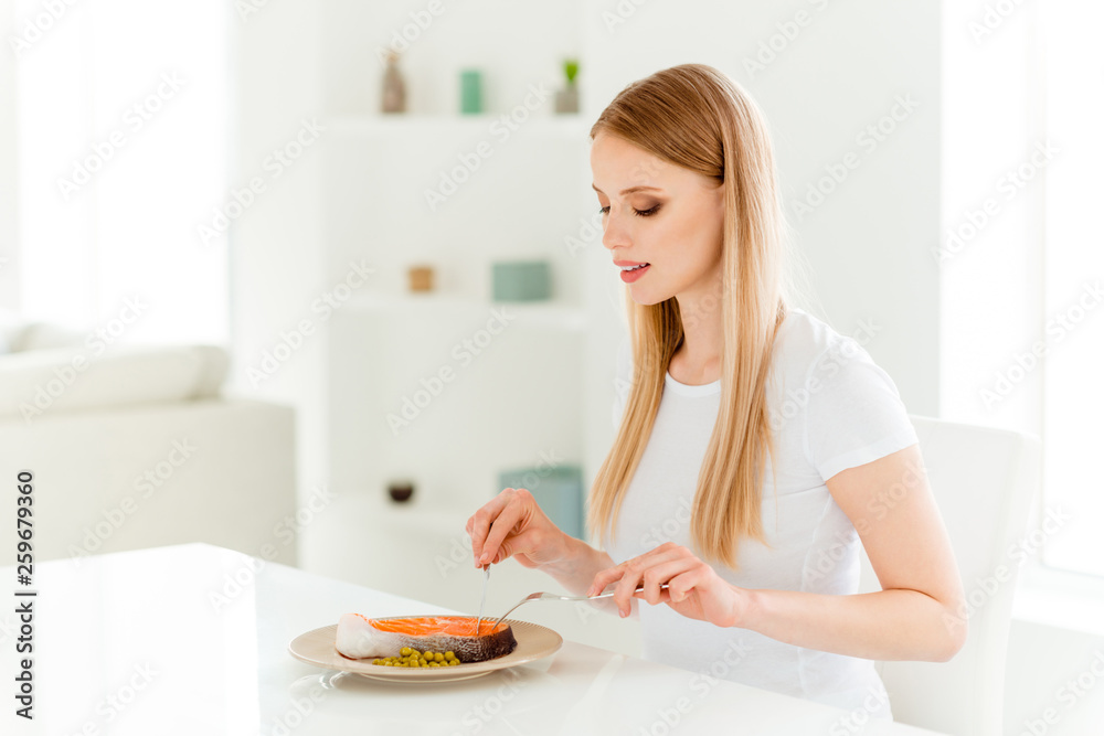 Portrait of calm positive millennial youth enjoy have dinner snack use fork knife eat delicious dish with proteins starving sit table chair in modern kitchen wear cotton t-shirts