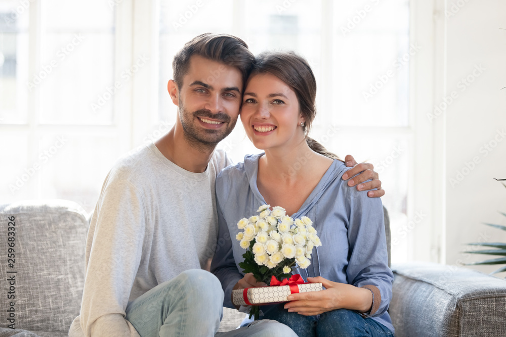 Happy couple sitting on couch with flowers and gift box