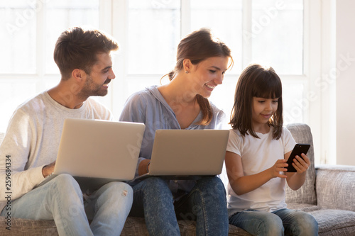 Smiling family sitting on couch absorbed in digital devices