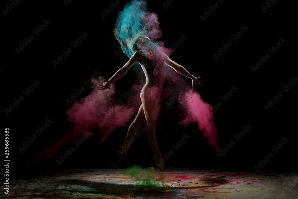 Fototapeta Slim girl jumping in color dust cloud in the dark