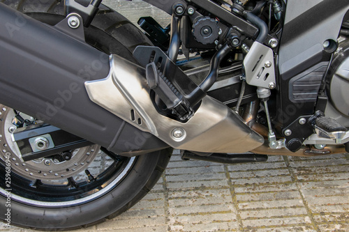 Parte lateral trasera de una moto mostrando una parte de la rueda y el tubo de escape.