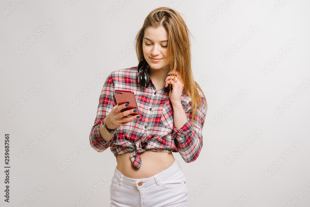 Young caucasian woman wearing shorts and shirt holding smartphone on grey background Young caucasian woman wearing shorts and shirt holding smartphone on grey background