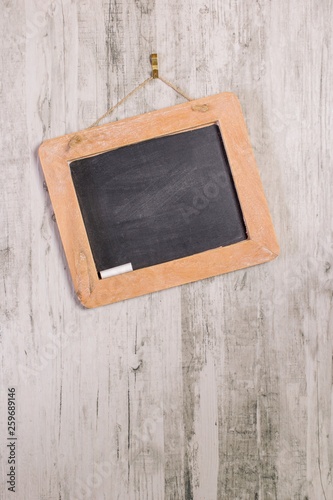 A wooden framed blackboard with chalk hanging at an angle on a rustic background with copy space for your text or picture