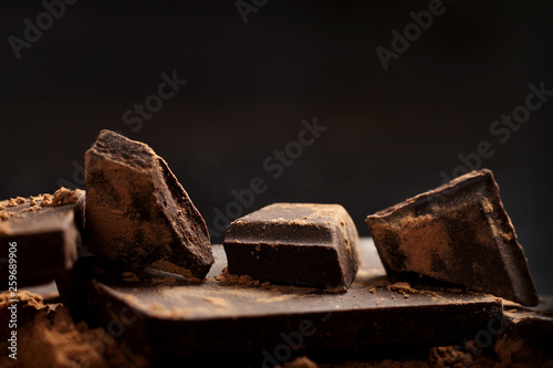 Broken dark chocolate and cocoa on black background.