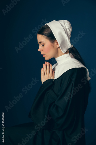 Talking to the moon at night. Medieval young woman as a nun in vintage clothing and white mutch sitting on the chair on dark blue background. Concept of comparison of eras. photo