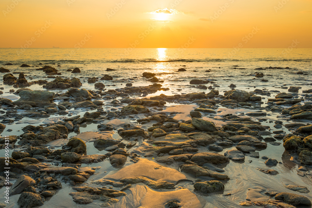 Beautiful colorful sunset landscape with sand beach, golden sun and stones at sea shore