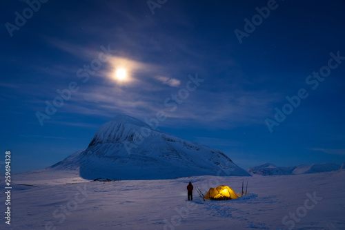 Fotografi Man looking at the night sky while camping at the snow covered mountains in Sarek National Park