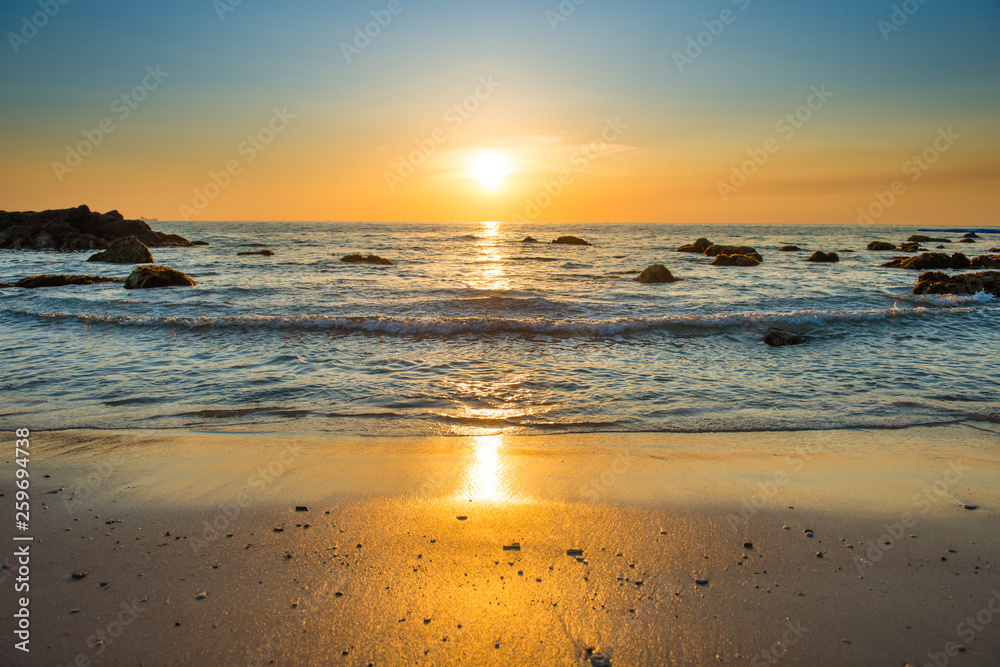 Beautiful colorful sunset landscape with sand beach, golden sun and stones at sea shore