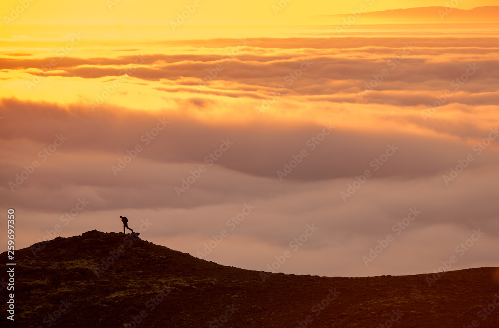 Silhouette of a man on the ridge above the sea of clouds, misty mountains at sunset in Iceland Silhouette of a man on the ridge above the sea of clouds, misty mountains at sunset in Iceland
