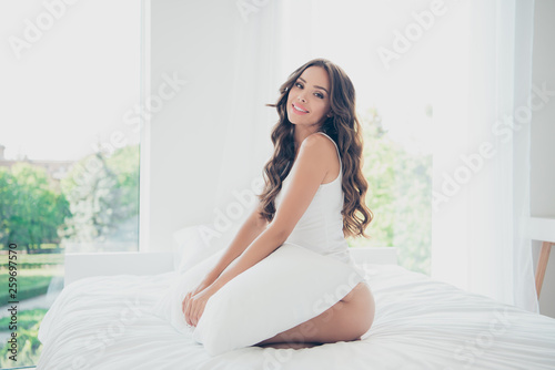 Profile side view portrait of her she nice-looking sweet adorable fascinating attractive charming cute lovely cheery tender wavy-haired lady sitting on bed hugging pillow in light white interior room