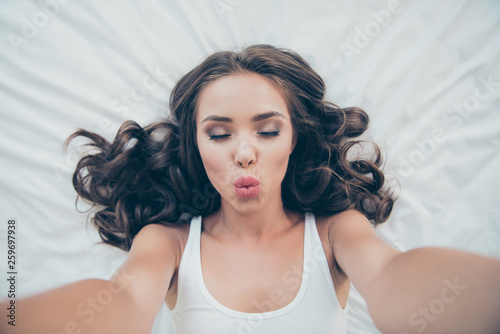 Self-portrait of nice-looking sweet tender gentle winsome attractive charming cute lovely lovable wavy-haired lady lying on bed waiting boyfriend husband soulmate in light white interior room indoors