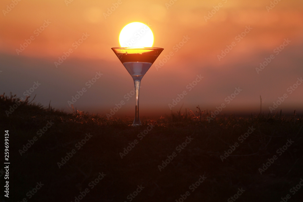 Fototapeta premium Silhouette of martini glass on sunset background, setting sun in a glass
