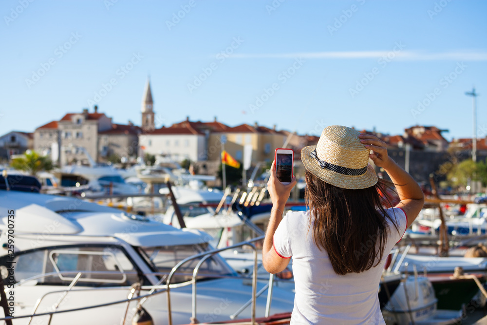 Young travelling woman in hat taking photos of summer sunny sea with smartphone camera. Brunette girl making photography on summer vacation