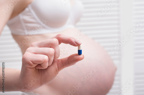 Pregnant woman in underwear holding a pill in her hand on a light background