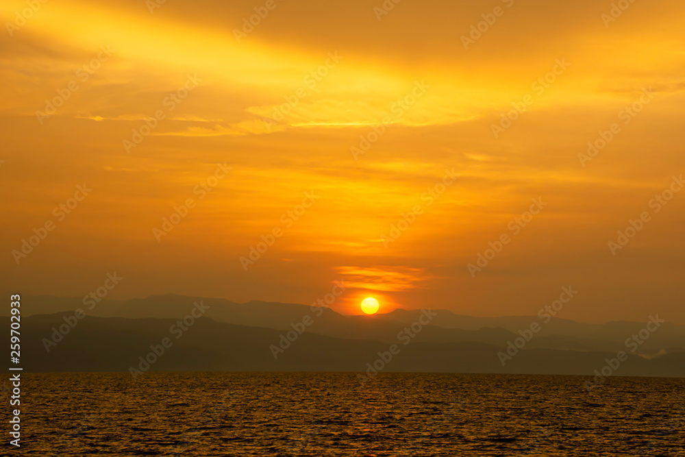 Golden light of sunrise behind the mountains and the sea.