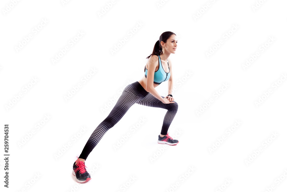 A dark-haired woman coach in a sporty short top and gym leggings makes lunges by the feet side, hands are held out to the side on a white isolated background in studio A dark-haired woman coach in a sporty short top and gym leggings makes lunges by the feet side, hands are held out to the side on a white isolated background in studio