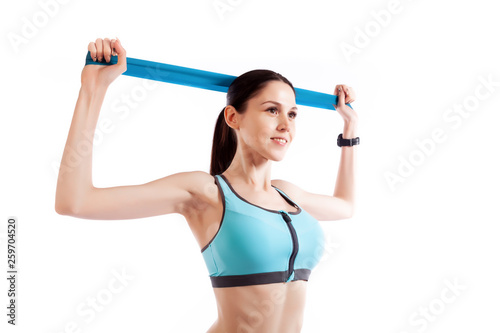 A dark-haired woman coach in a sporty short top and gym leggings exercise for your back, hands behind his head breeding with sport fitness rubber bands on a  white isolated background in studio