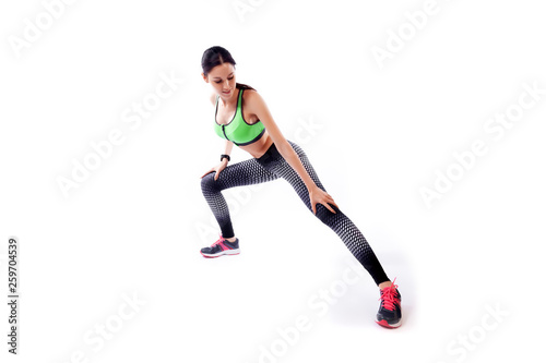 A dark-haired woman coach in a sporty  short top and gym leggings makes lunges  by the feet side, hands are held out to the side   on a  white isolated background in studio © Виталий Сова
