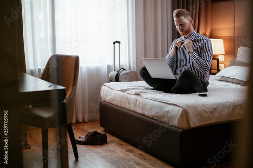 Man working on his laptop. Executive manager talking on the phone while working on his laptop. Businessman sitting on the bed working. © JustLife
