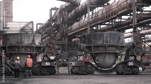 Metal melting vats being transported on big carts to the metal melting shop, heavy industry concept. Stock footage.Two male workers in uniform standing outdoors at the metal smelting plant. photo