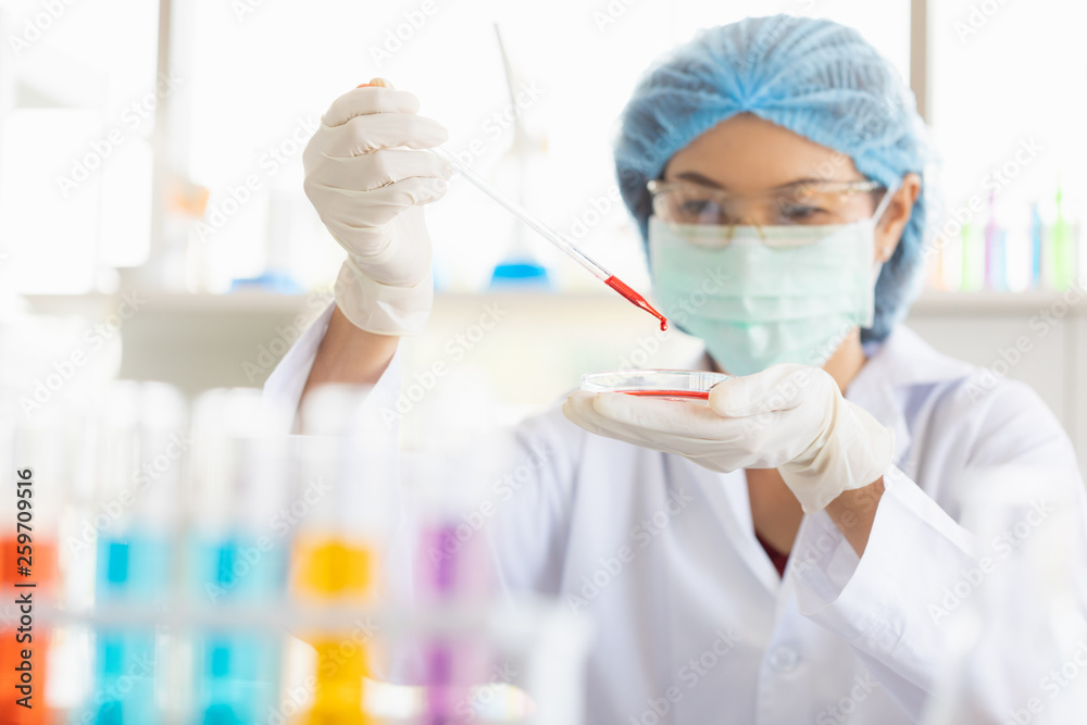 Female scientist dropping red liquid into beaker.. Female scientist dropping red liquid into beaker..