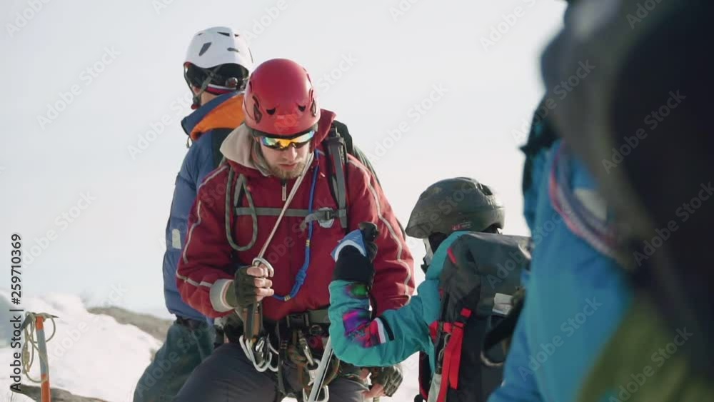 climber helps his friend and fastens to his carbine and checks the mount. the whole group is preparing to descend. climber helps his friend and fastens to his carbine and checks the mount. the whole group is preparing to descend.