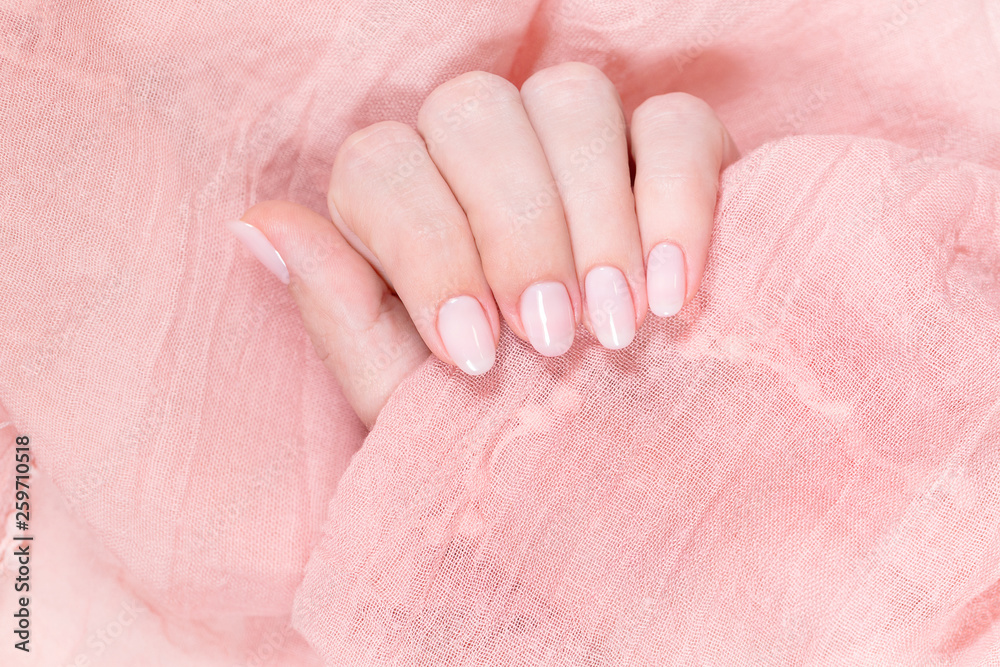 Top view closeup of two female hands isolated on pink cloth background. Fingernails with beautiful natural pink manicure. Horizontal color photography.